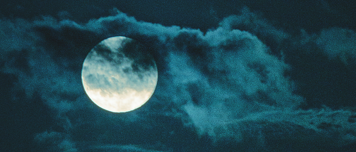 Full moon glowing through dark clouds in a night sky, symbolising reflection and release during the Pisces lunar eclipse.