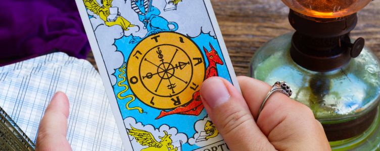 Hand holding the Wheel of Fortune tarot card with a deck on a wooden table beside a lantern — a simple one-card draw for daily guidance.