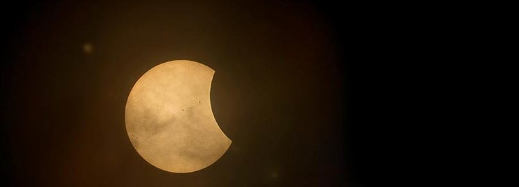 A darkened sun with a glowing golden crescent visible, captured during a partial solar eclipse.