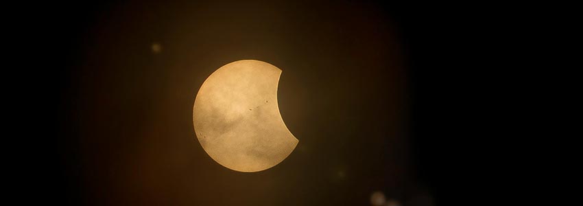 A darkened sun with a glowing golden crescent visible, captured during a partial solar eclipse.